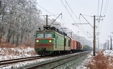 Old Soviet electric locomotive with a long freight train in winter in Kyiv Oblast of Ukraine