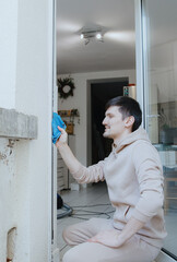 One young man washes a window frame with a blue rag.