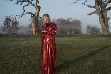 Young beautiful slender woman in a fashionable red dress. Woman posing in the fog morning sunrise...