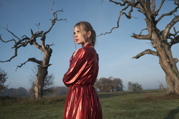 Young beautiful slender woman in a fashionable red dress. Woman posing in the fog morning sunrise...