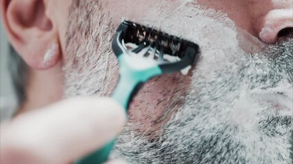 Close up of a man shaving his beard with a razor