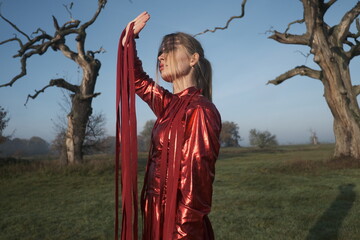 Young beautiful slender woman in a fashionable red dress. Woman posing in the fog morning sunrise...