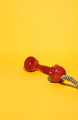 A vintage red telephone handset lies on a vibrant yellow background, creating a striking retro...