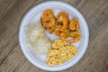 Take-out order of shrimp curry served with rice and macaroni salad on a paper plate