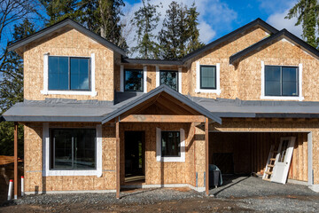 New home construction, house exterior with wood OSB, oriented strand board, walls up and windows installed and roof base layer and moisture barrier on, sunny winter day on the job site
