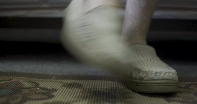 Person's feet slipping into slippers next to bed - low, close up