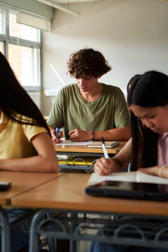 Concentrated high school male student taking a written test in a classroom. University people working diligently on their exam papers. Vertical image with copy space.