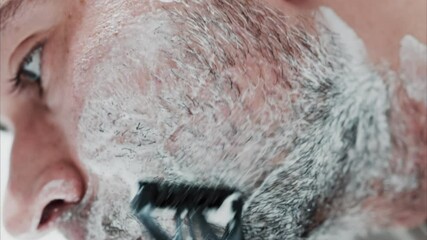 Close up of a man shaving his beard with a razor