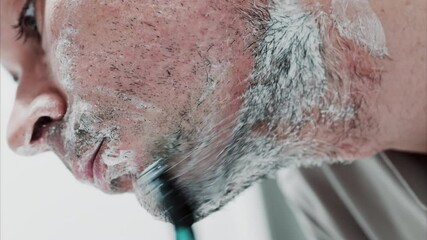 Close up of a man shaving his beard with a razor