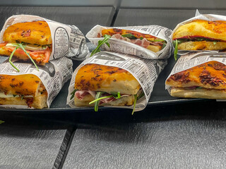 focaccia sandwiches in paper on black plate in sales display on a wooden plate italian street food
