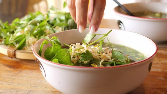 Freshly made pho soup is garnished with bean sprouts and basil leaves Woman adds ingredients that enhance flavor of hot Asian soup Traditional Vietnamese soup with fragrant broth and fresh herbs