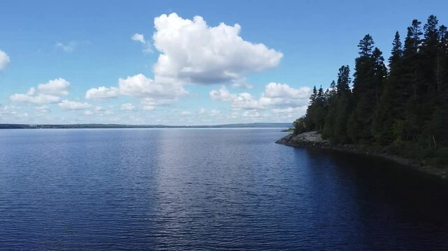 Elevated flight over the rocky shore of Lake Matapedia,Quebec,Canada, a large freshwater lake under a blue sky dotted with clouds