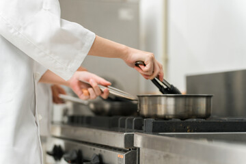ガスコンロでフライパン調理するシェフの女性（手元）
