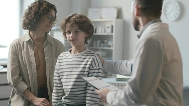 Mother and little son sitting on examination table, talking and listening attentively to pediatrician as getting medical consultation in modern clinic