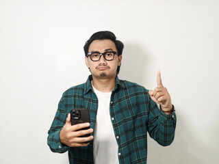 Sadness young handsome Asian man wearing a plaid shirt pointing finger up when holding mobile phone isolated on white background