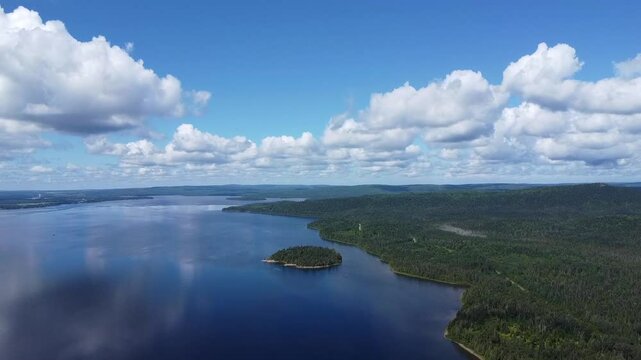 Panoramic aerial view showing a tranquil lake dotted with islands surrounded by lush green forests under a bright blue sky with fluffy clouds. Lac Matapedia,Quebec,Canada.