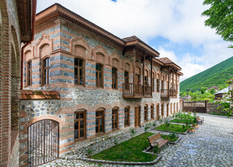 Fototapeta premium Exterior view of Shaki Khan's Mosque Complex, a historic structure located in Shaki, Azerbaijan. The complex is characterized by its stone walls, wooden balconies, and traditional architecture