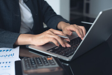 Business woman accountant working on laptop computer, analyzing financial report with business document and calculator on office table. 