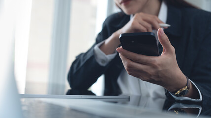 Business woman using mobile smart phone, searching the information during working on laptop computer with digital tablet on office table. Businesswoman surfing the internet on smartphone