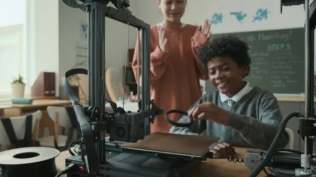 Two classmates feeling excited, using 3D printer for first time during 3D modelling class at modern school