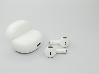 A pair of white wireless earphones with an open case, featuring a modern, elegant and minimalist design, on a white background.