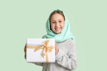 Little Muslim girl with gift on light background