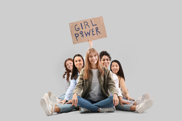 Beautiful young happy women holding paper with text GIRL POWER and sitting on grey background....