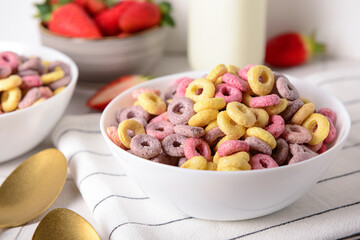 Bowls with colorful sweet cereal rings and strawberries on white tile table