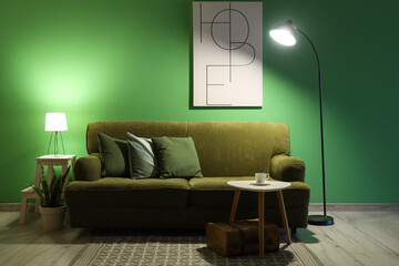 Sofa, table with cup of coffee and glowing lamps in interior of living room