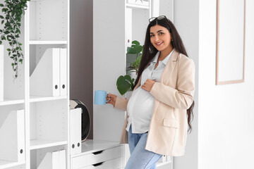 Pregnant businesswoman with cup of coffee in office