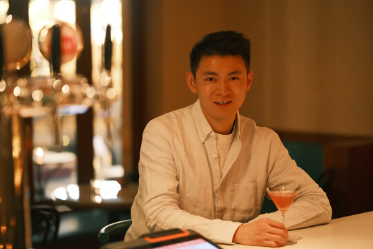 handsome East Asian young man sitting at night bar counter, looking at camera