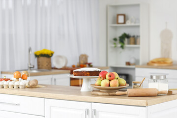 Stand with tasty pie, apples and rolling pin on table in kitchen