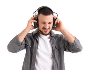 Young man in headphones suffering from loud noise on white background