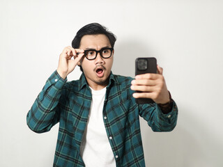 Adult Asian man looking to his phone with surprised expression isolated on white background
