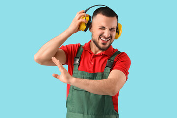 Male worker with hearing protectors suffering from loud noise on blue background