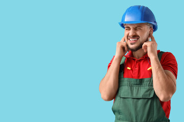 Male worker suffering from loud noise on blue background
