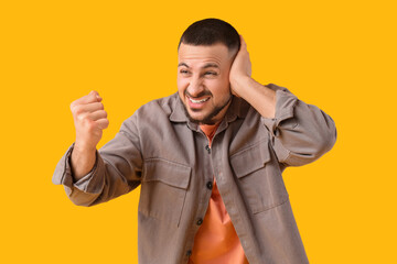 Young man suffering from loud noise on yellow background