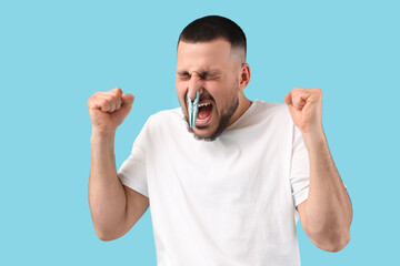 Fototapeta premium Stressed young man with clothespin on blue background. Stuffy nose concept