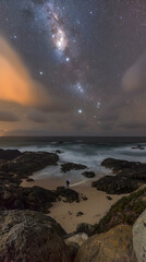 Solitary figure stargazing on a rocky beach at night, Milky Way visible, ocean waves. Ideal for travel, adventure, and nature websites