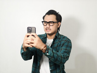 Adult Asian man is typing on his mobile phone with angry expression isolated on white background