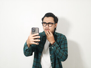 Worried young Asian man wearing a plaid checkered shirt reading news on a phone while biting nails...