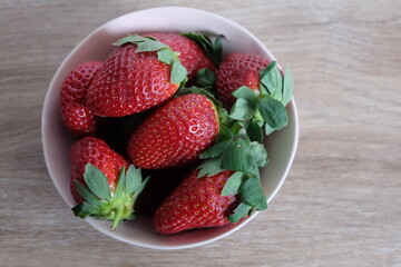 Washed strawberries in a pink bowl with a background of wood