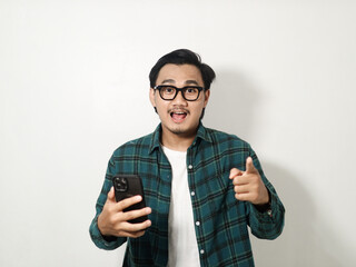 happy asian man is holding mobile phone while pointing to camera isolated on white background