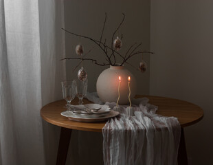 Easter bouquet with eggs decor in a ceramic vase, candles, dishes on a round wooden table
