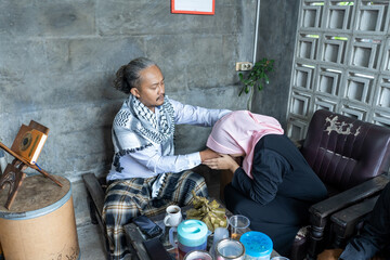 Senior men with long hair sit on the sofa with their younger guests and kiss their hands. Asian Muslim traditions on Eid al-Fitr