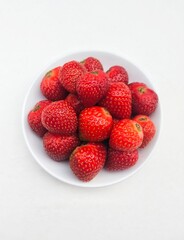 Close-up of strawberries in a small white plate on a white background. 