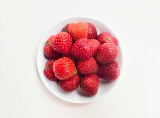 Close-up of strawberries in a small white plate on a white background. Top of view. 