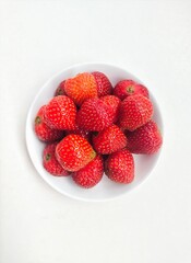 Strawberries in a small white plate on a white background. Top of view. 
