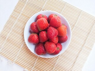 Directly above shot of strawberries in a small white plate on a white background. Top of view. 