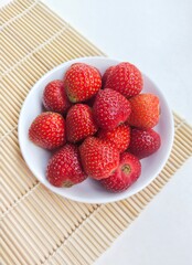 Strawberries in a small white plate on a white background. Top of view. 